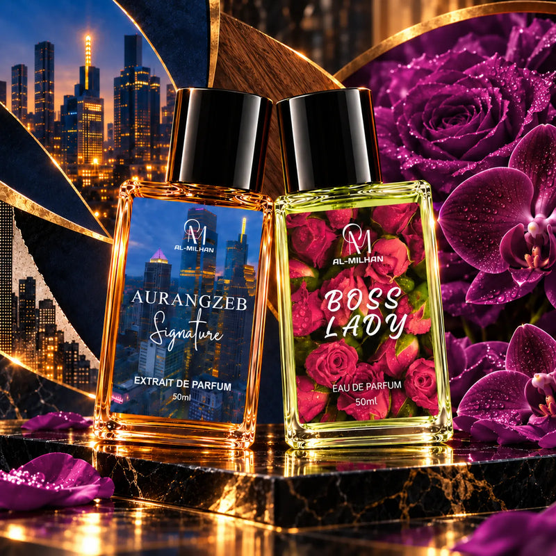 Amber Aurangzeb and pale green Boss Lady, two 50ml bottles leaning together as a couple on shared black marble, with navy city, cedar, brass and raspberry-purple rose and orchid graphics. Boss Lady keeps its original red rosebud label and italic lettering.